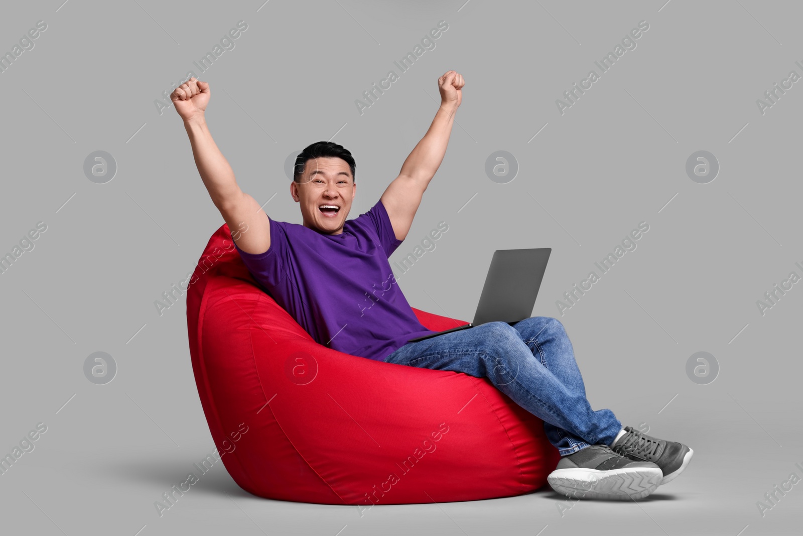 Photo of Emotional man with laptop sitting in beanbag chair against grey background