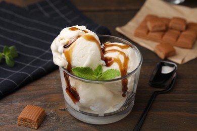 Photo of Scoopsice cream with caramel sauce, mint leaves and candies on wooden table, closeup
