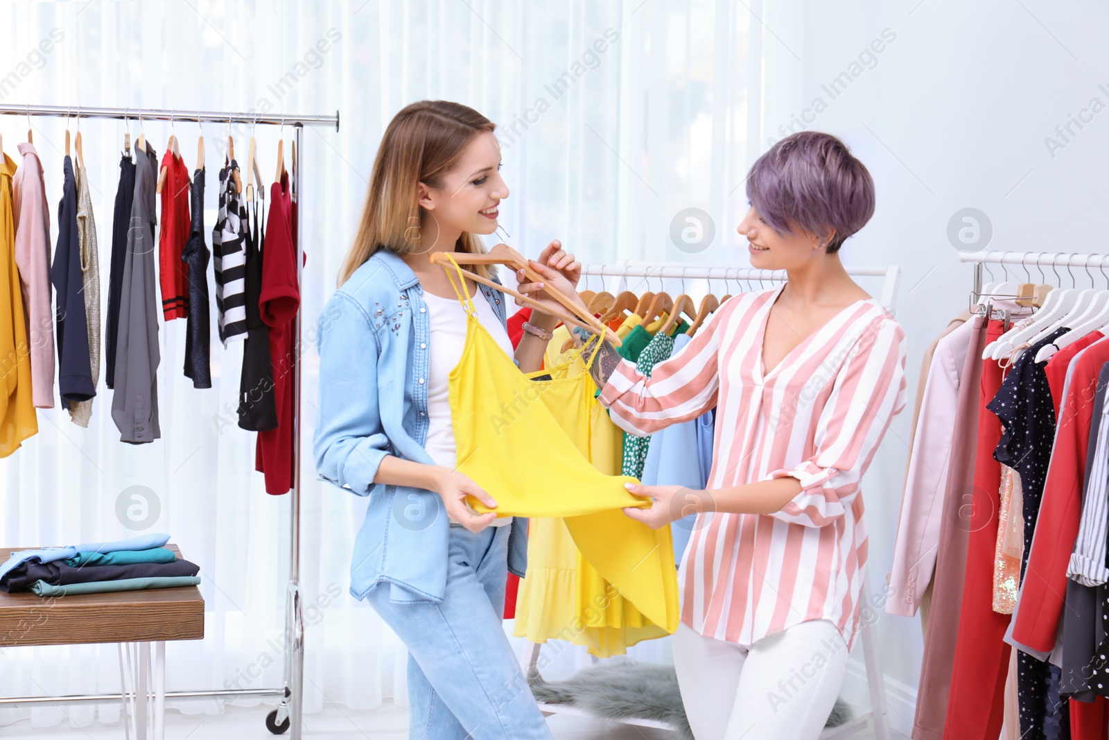 Photo of Young stylist helping customer to choose clothes indoors