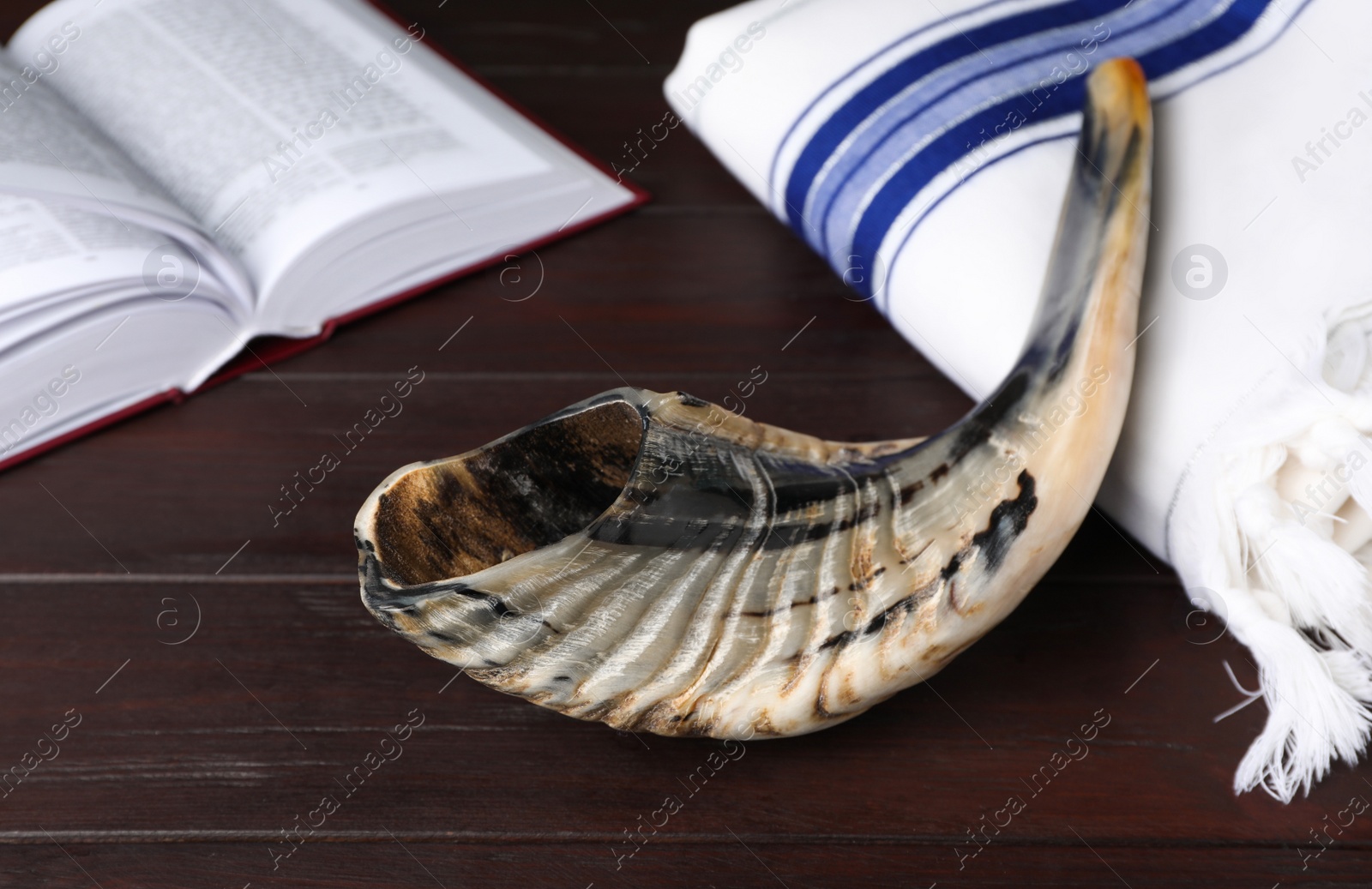 Photo of Shofar, Tallit and open Torah book on wooden table. Rosh Hashanah holiday attributes