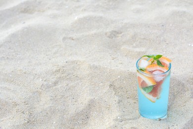 Photo of Glass of refreshing drink with grapefruit and mint on sandy beach, space for text