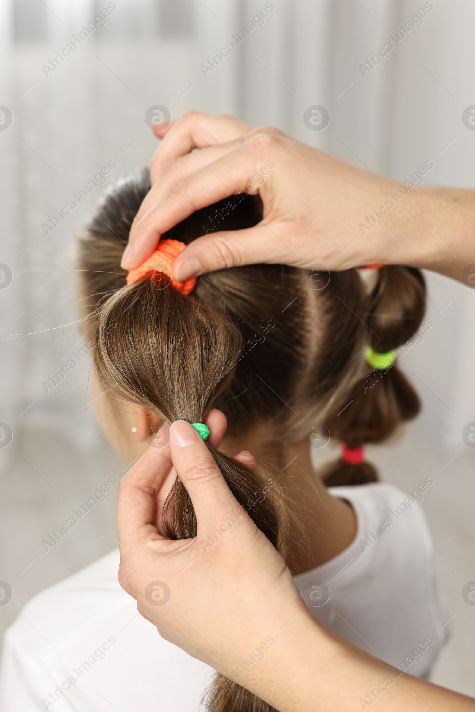 Photo of Professional stylist braiding girl's hair indoors, closeup