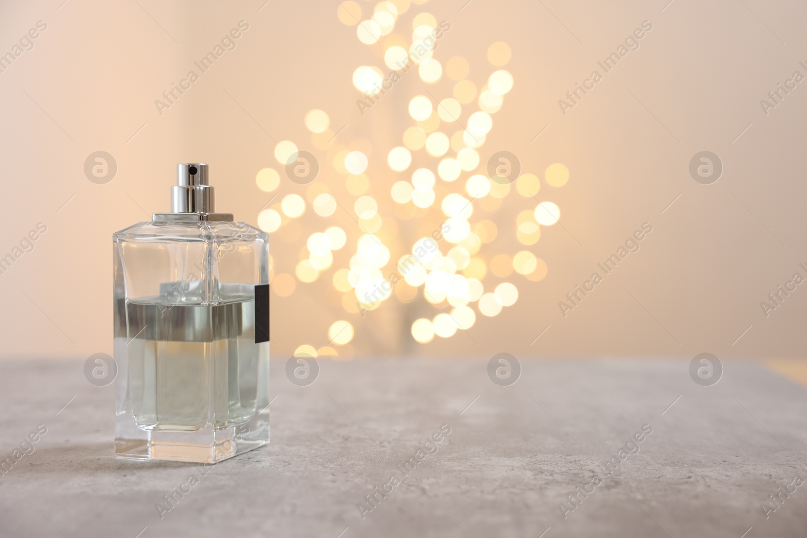 Photo of Bottle of perfume on table against beige background with blurred lights, space for text