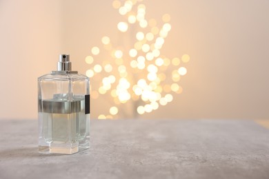 Photo of Bottle of perfume on table against beige background with blurred lights, space for text