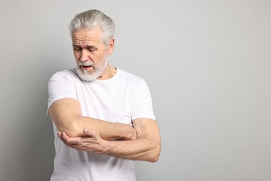 Photo of Arthritis symptoms. Man suffering from pain in elbow on gray background, space for text