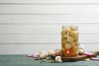 Glass jar of pickled mushrooms and ingredients on light blue wooden table. Space for text
