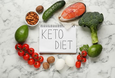 Photo of Notebook with words Keto Diet and fresh products on white marble table, flat lay