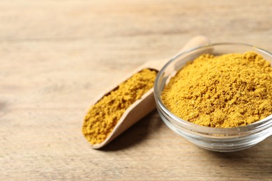Photo of Curry powder in bowl and scoop on wooden table, closeup. Space for text