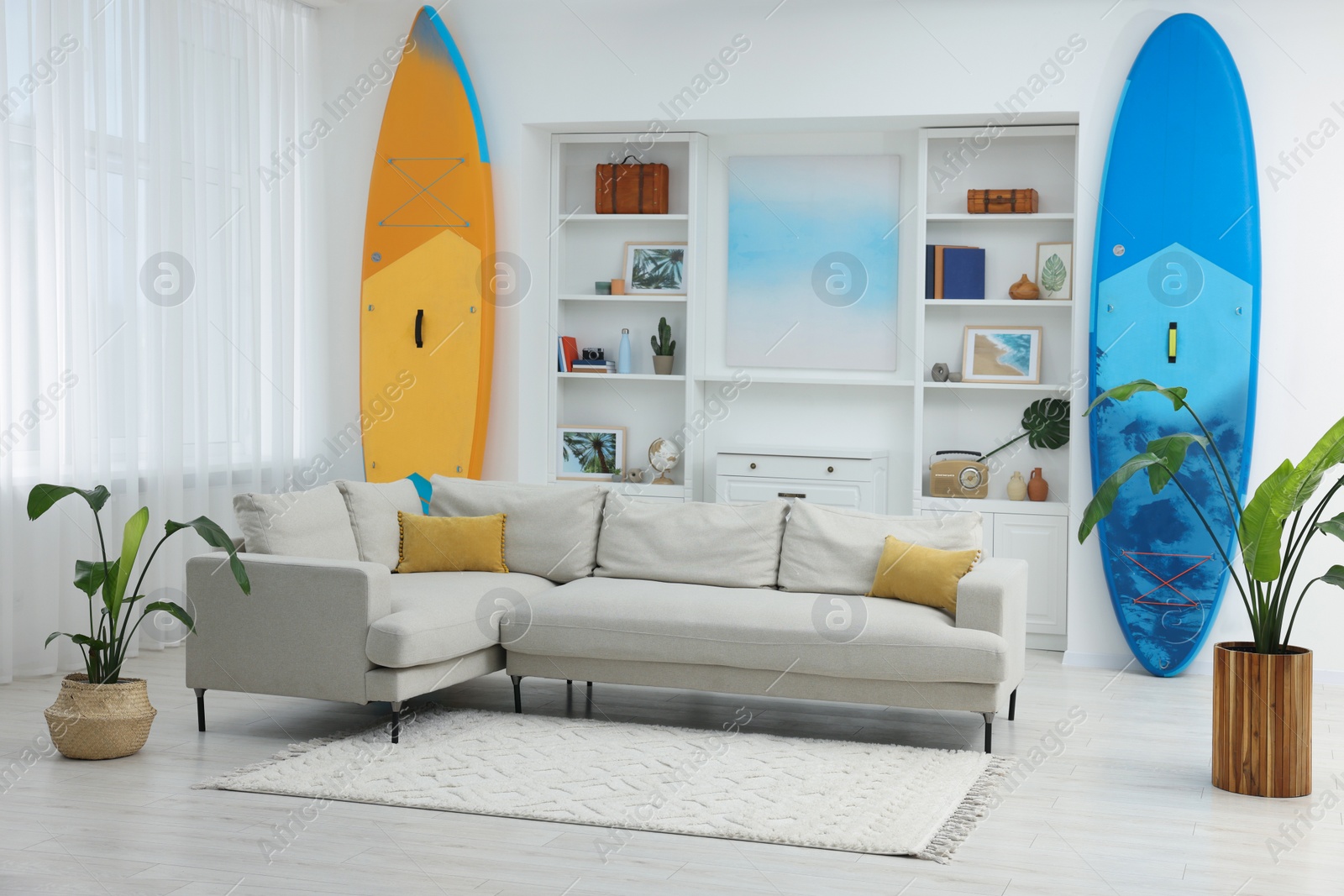 Photo of SUP boards, shelving unit with different decor elements and stylish sofa in room. Interior design