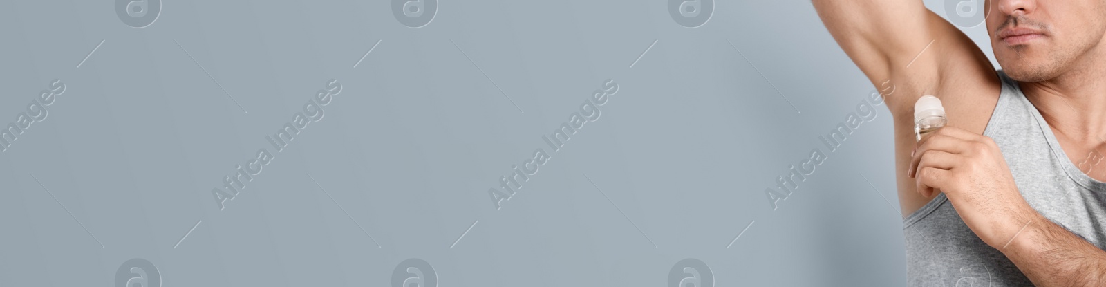 Photo of Man applying deodorant to armpit on grey background, closeup. Space for text