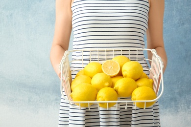 Photo of Woman holding wire basket with lemons against color background