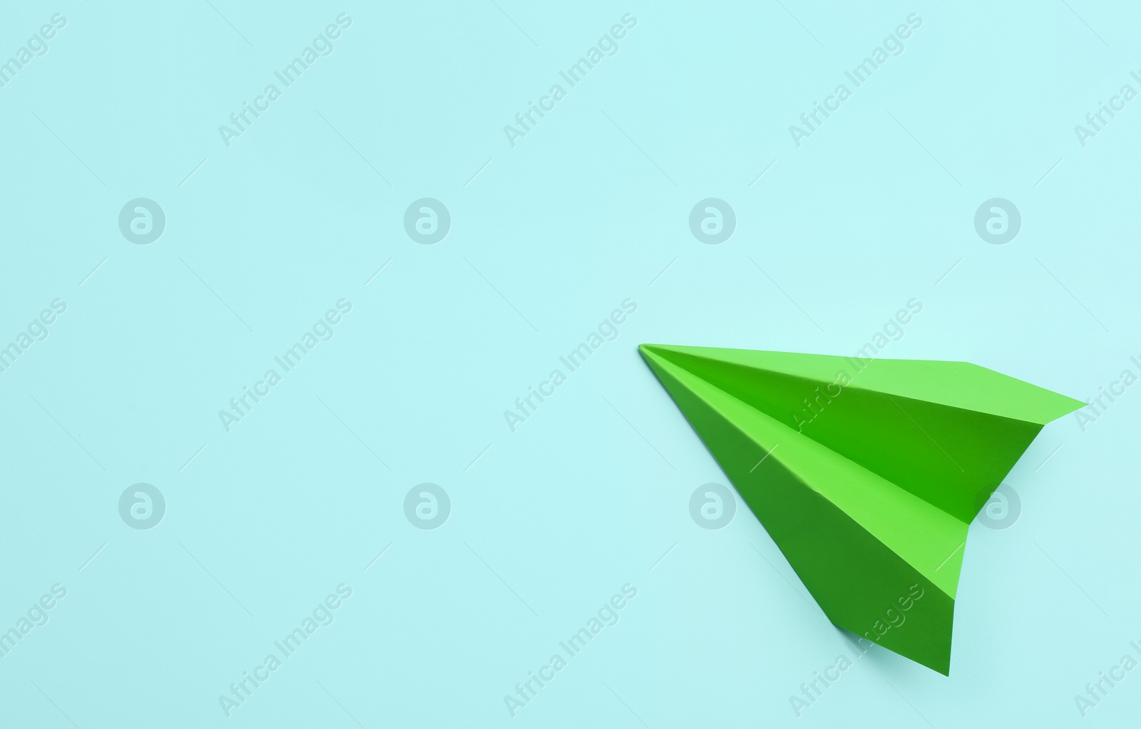 Photo of Green paper plane on light blue background, top view. Space for text