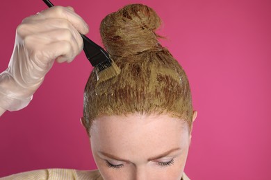 Photo of Young woman dyeing her hair with henna on pink background, closeup