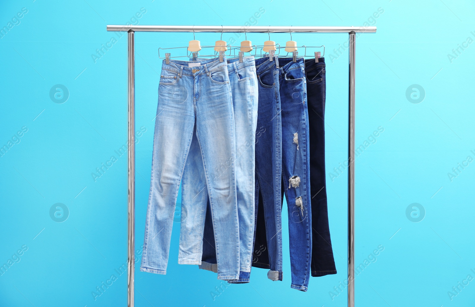 Photo of Rack with stylish jeans on color background