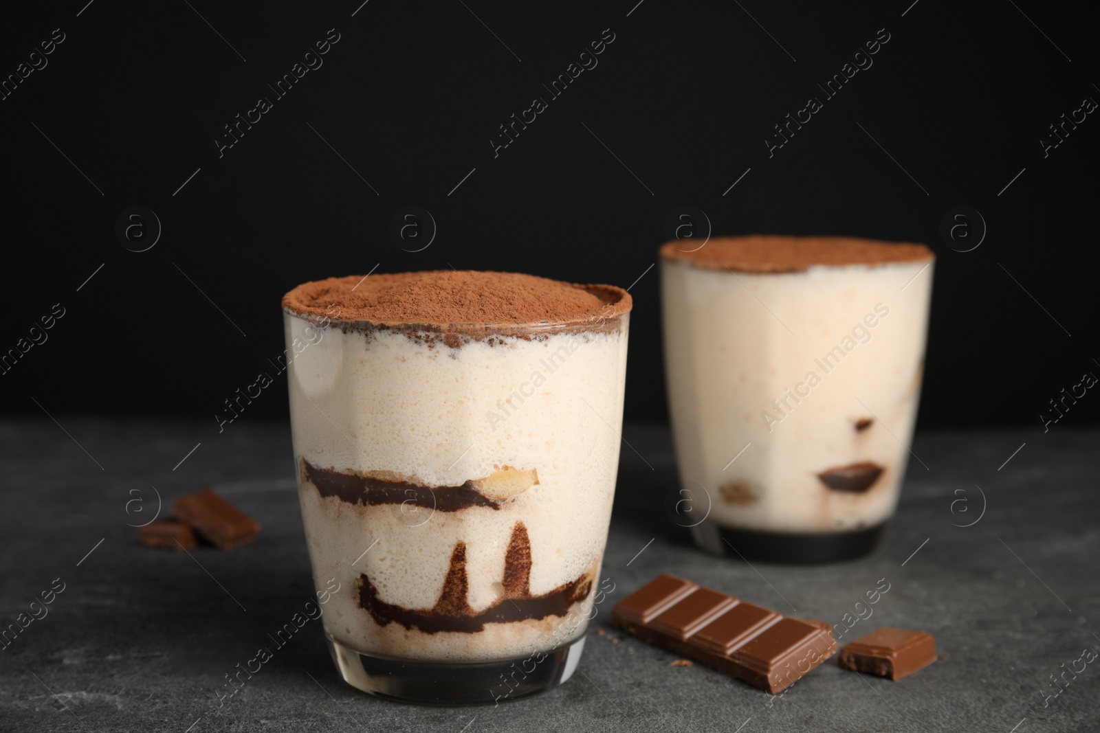 Photo of Two glasses of tiramisu cake on table against dark background