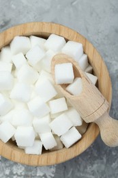 White sugar cubes in wooden bowl and scoop on grey table, top view