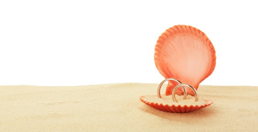 Photo of Honeymoon concept. Two golden rings in shell and sand isolated on white