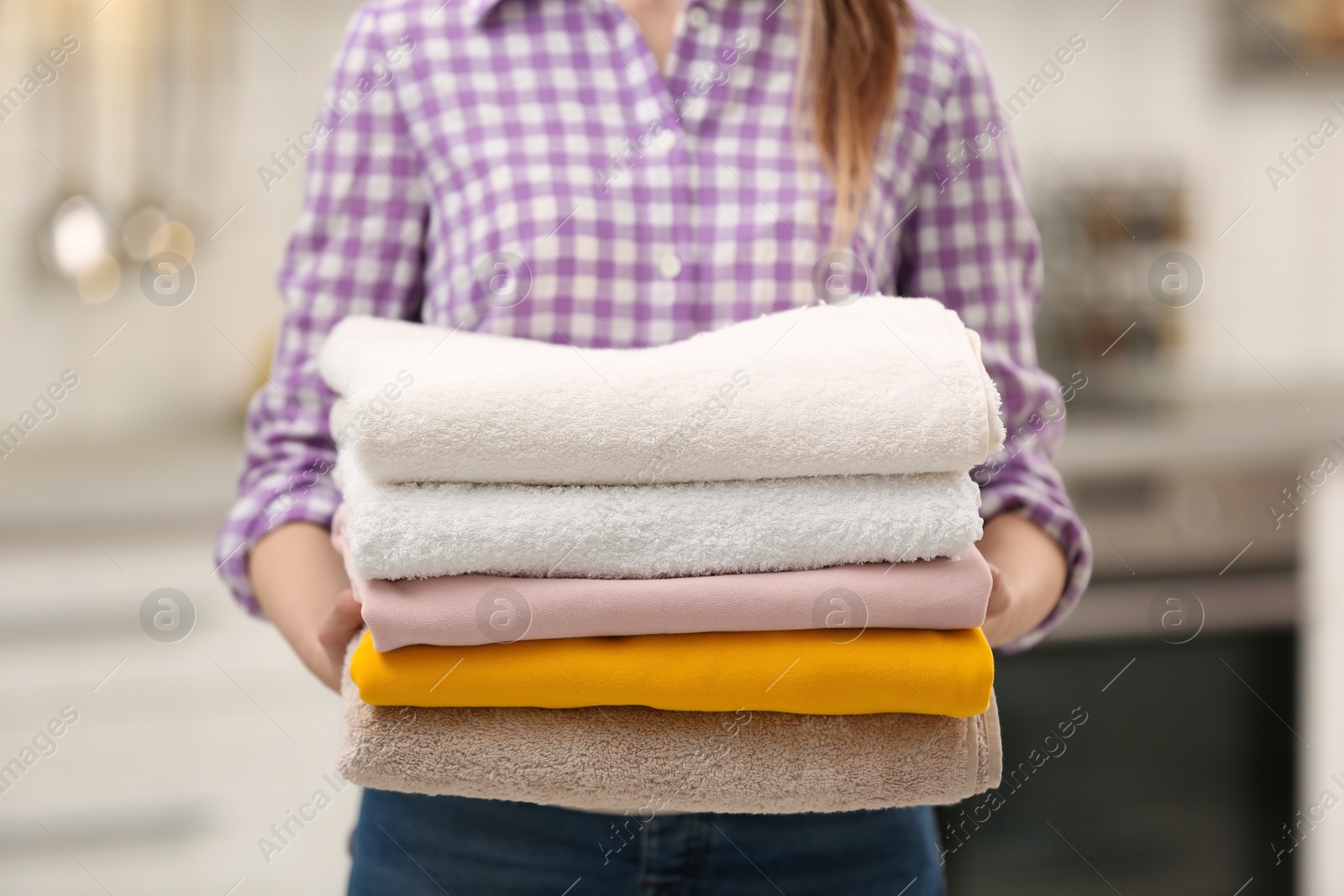 Photo of Woman holding stack of colorful towels in kitchen, closeup. Laundry day