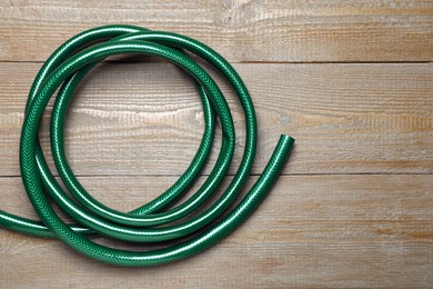 Green garden hose on wooden table, top view. Space for text