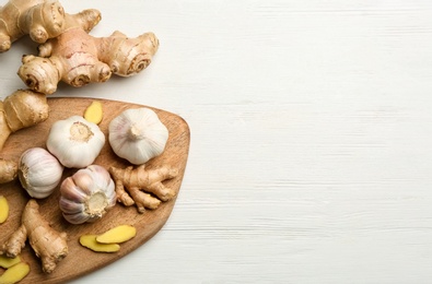 Flat lay composition with ginger, fresh garlic and space for text on white wooden table. Natural cold remedies