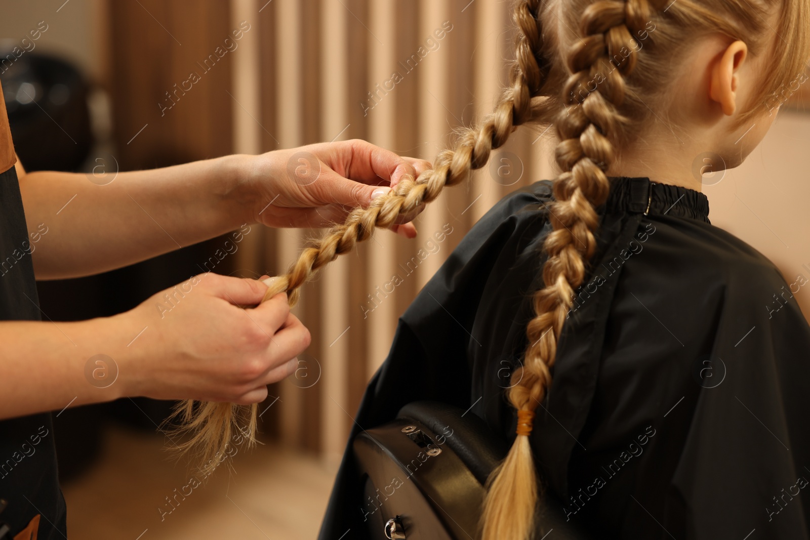 Photo of Professional hairdresser braiding girl's hair in beauty salon, closeup