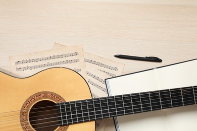Composition with guitar and music notations on light wooden table, flat lay. Space for text