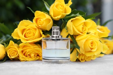 Perfume and beautiful bouquet of yellow roses on light table, closeup