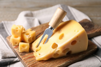 Photo of Tasty fresh cheese with fork on wooden board, closeup