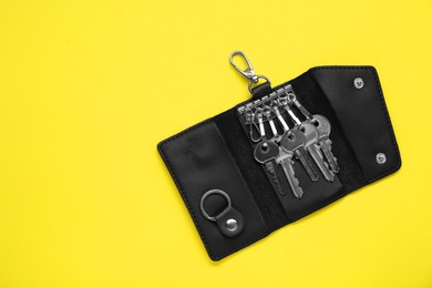 Open leather holder with keys on yellow background, top view. Space for text