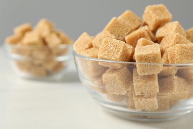 Photo of Brown sugar cubes in glass bowl on white table, closeup. Space for text
