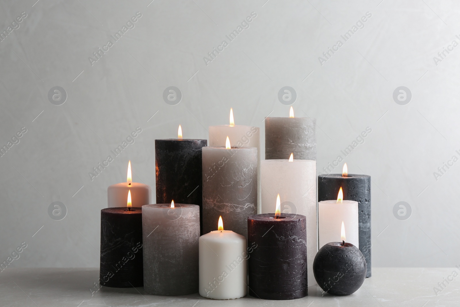 Photo of Set of burning candles on table against light background
