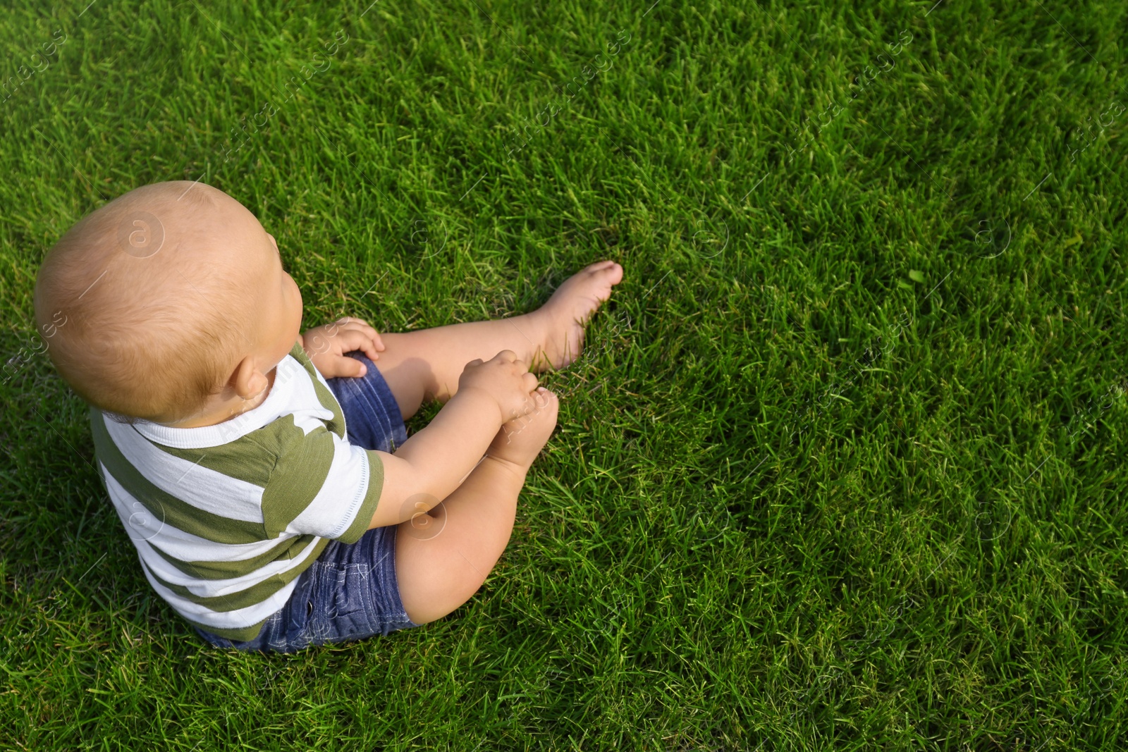 Photo of Adorable little baby sitting on green grass outdoors