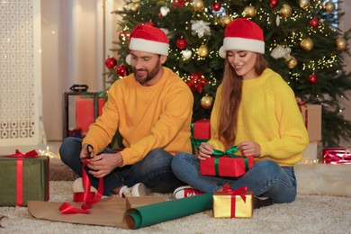Photo of Happy couple in Santa hats decorating Christmas gifts at home