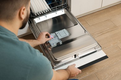 Photo of Man putting detergent tablet into open dishwasher, closeup