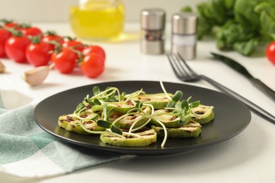 Photo of Delicious grilled zucchini slices and microgreens served on white table, closeup