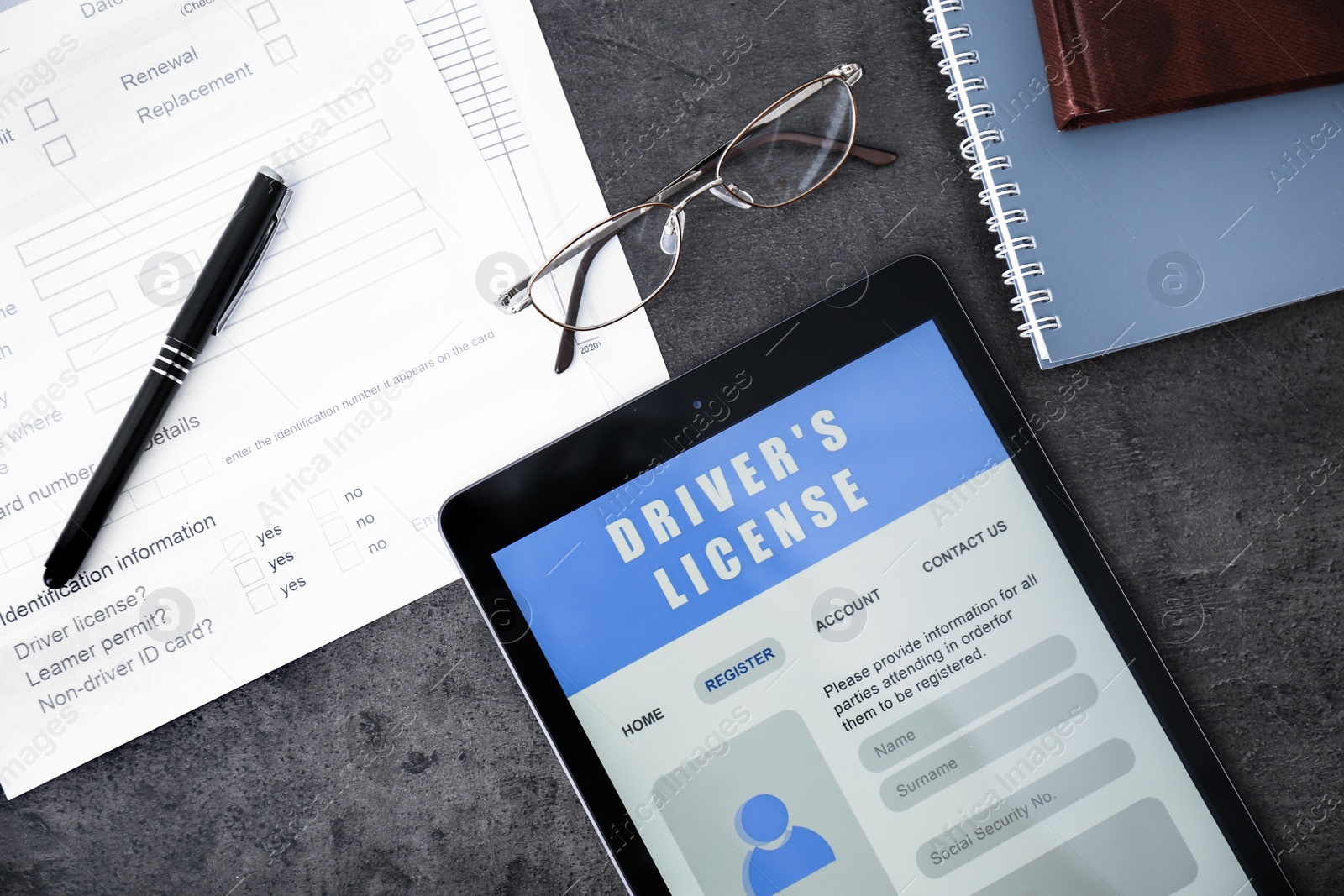 Photo of Tablet with driver's license application form, glasses and stationery on grey table, flat lay