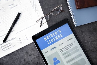 Tablet with driver's license application form, glasses and stationery on grey table, flat lay