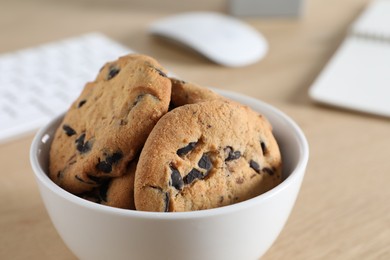 Photo of Chocolate chip cookies on wooden table at workplace, closeup