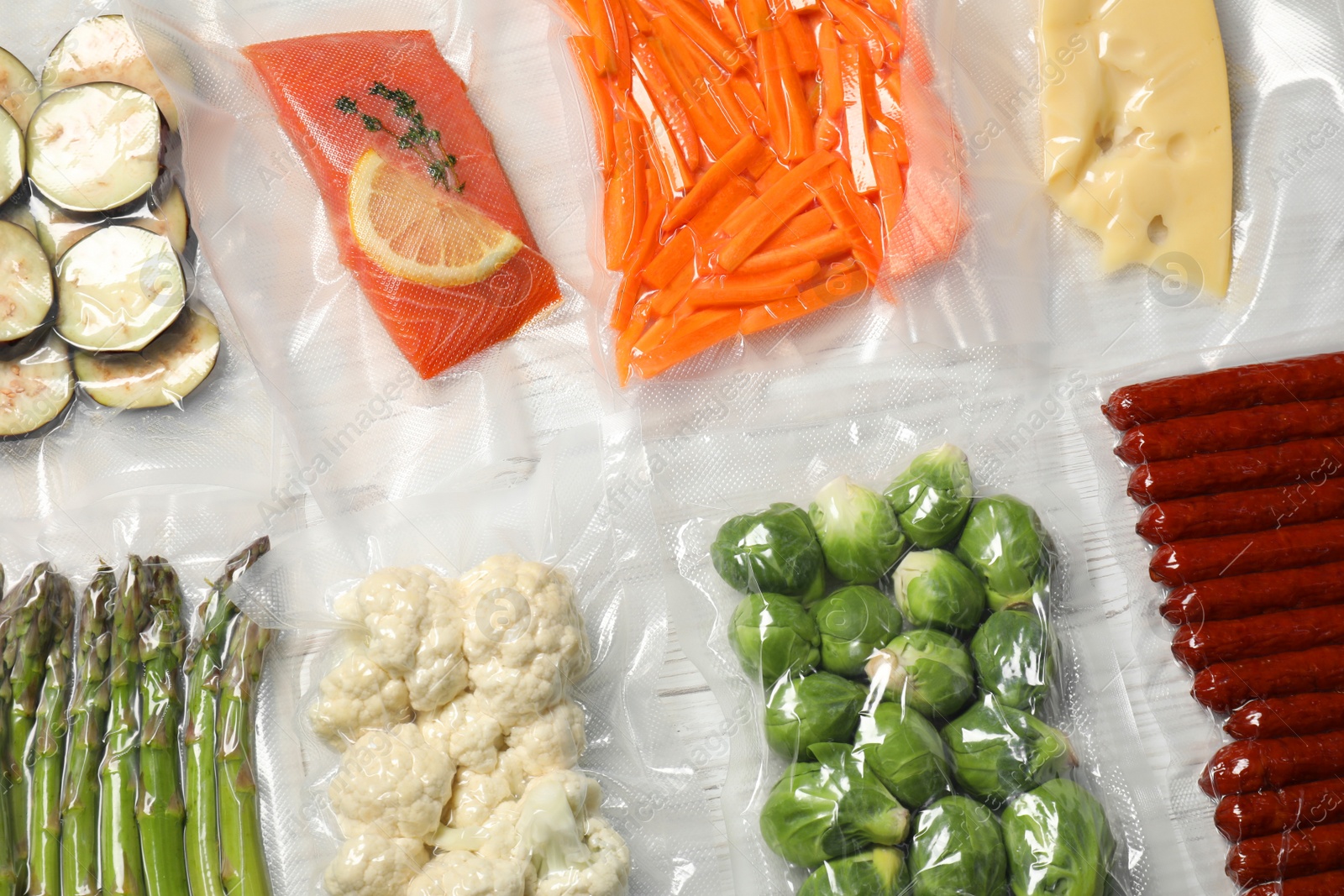 Photo of Different food products in vacuum packs on white wooden table, flat lay