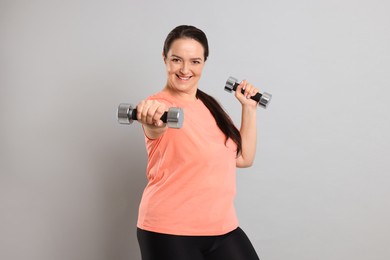Photo of Happy overweight woman doing exercise with dumbbells on grey background