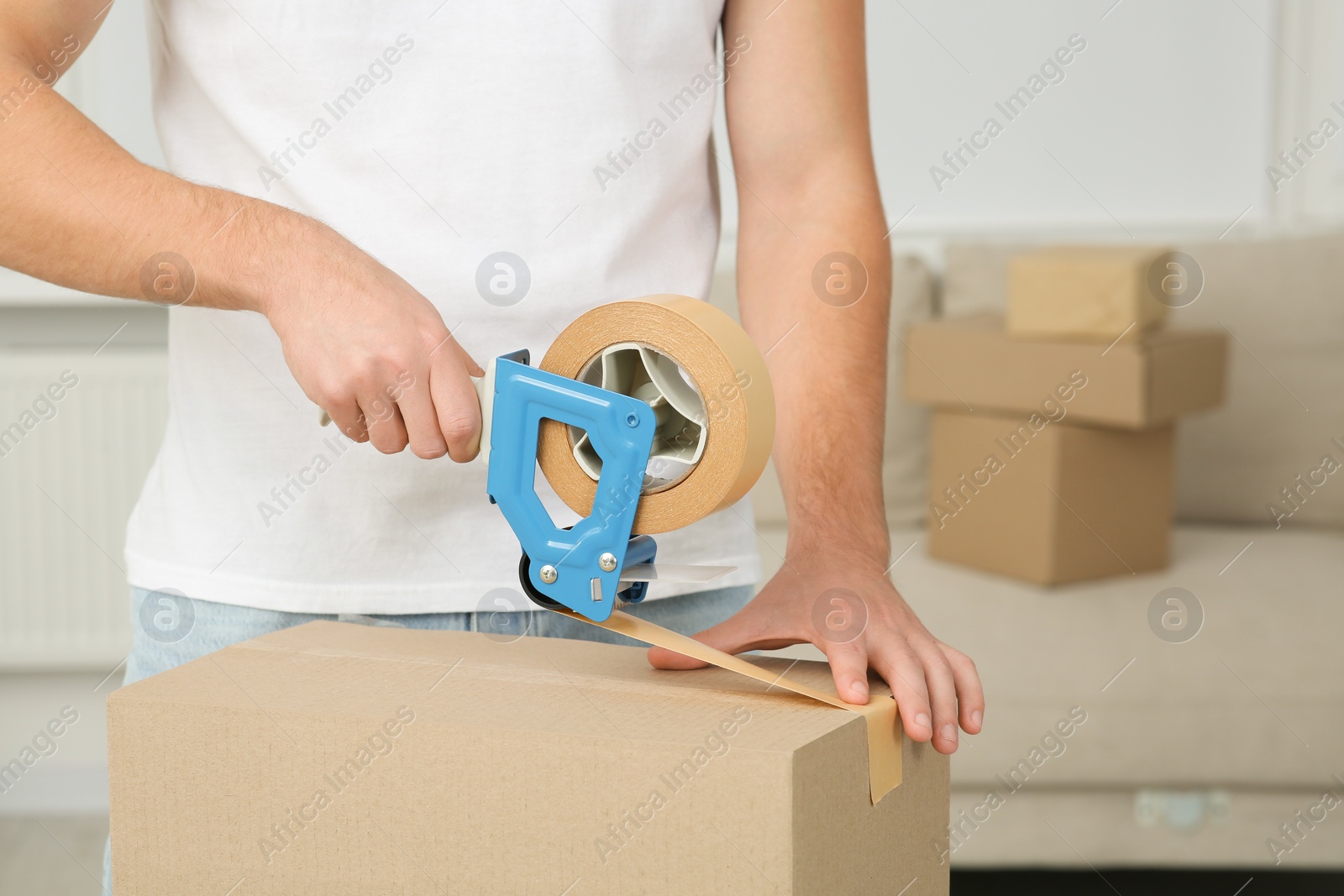 Photo of Man packing box with adhesive tape indoors, closeup