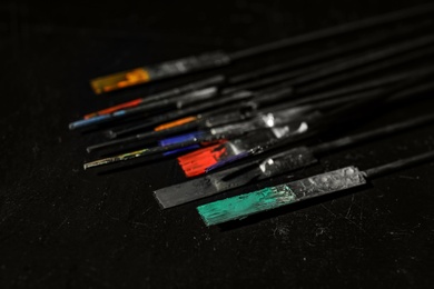 Photo of Tattoo needles covered with colorful inks on black background, closeup