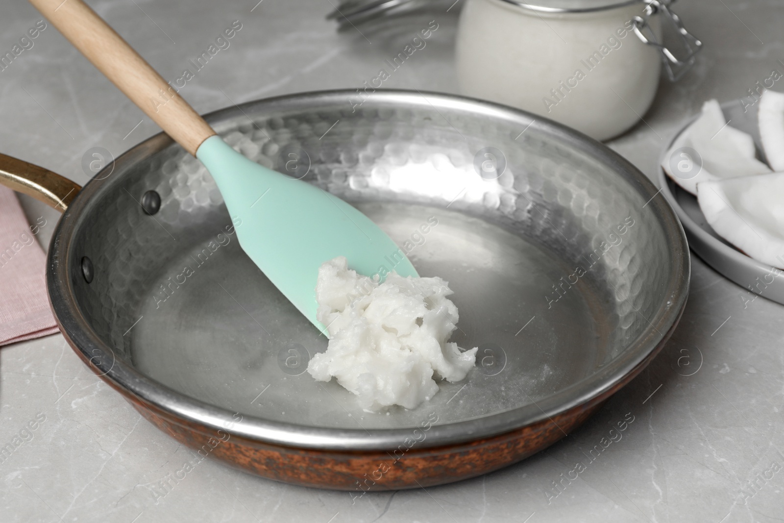 Photo of Frying pan with coconut oil and spatula on light grey table