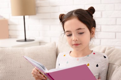 Photo of Little girl reading book on sofa at home