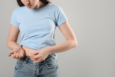 Photo of Diabetes. Woman making insulin injection into her belly on grey background, closeup. Space for text