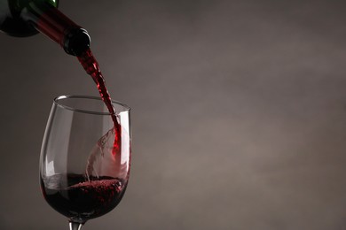 Photo of Pouring tasty red wine from bottle into glass on gray background, closeup. Space for text