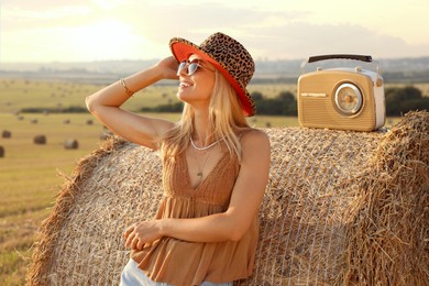 Photo of Happy hippie woman with receiver near hay bale in field