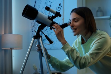 Beautiful young woman looking at stars through telescope in room