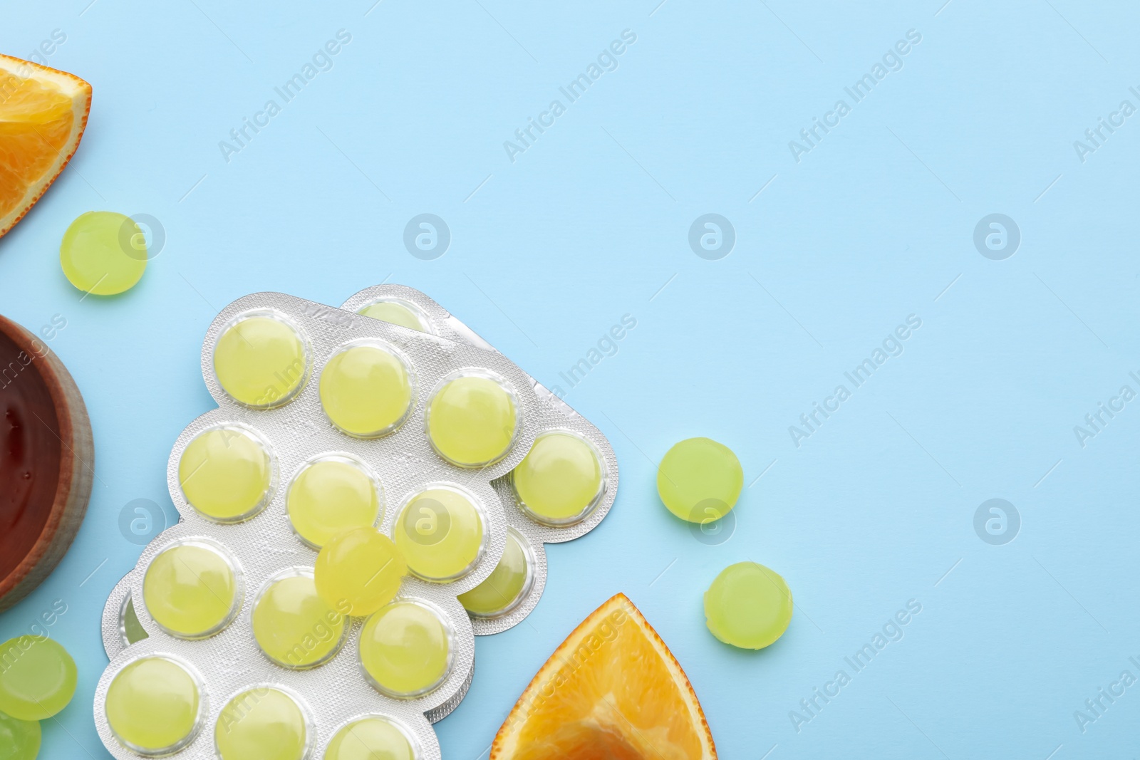 Photo of Many cough drops and slices of orange on light blue background, flat lay. Space for text