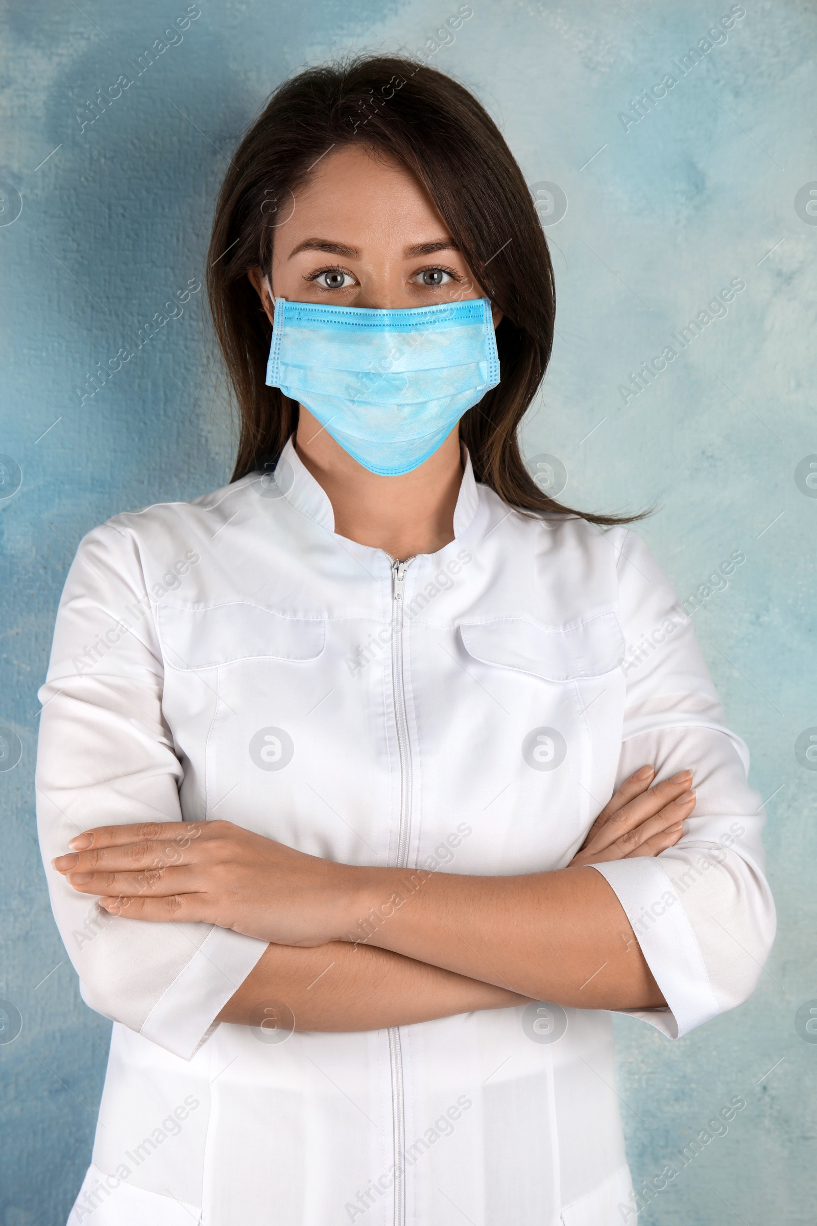 Photo of Doctor with disposable mask on face against light blue background